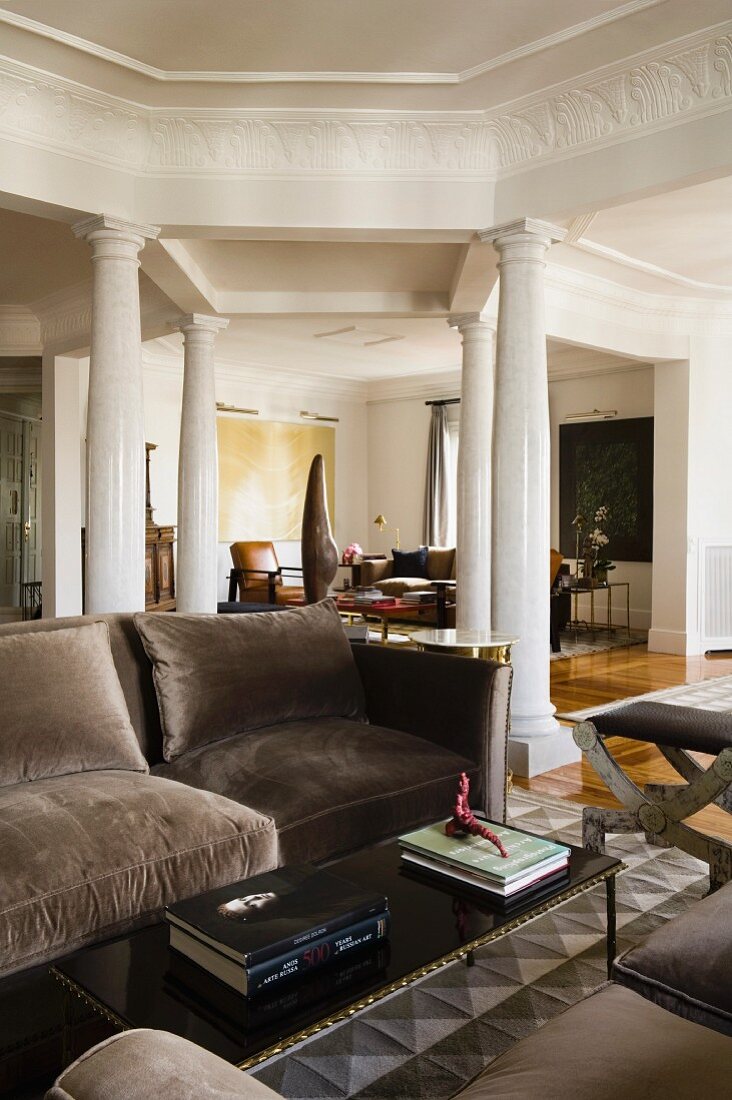 Sofa with grey velvet cover and coffee table in living room in front of square of columns under architraves with continuous stucco friezes