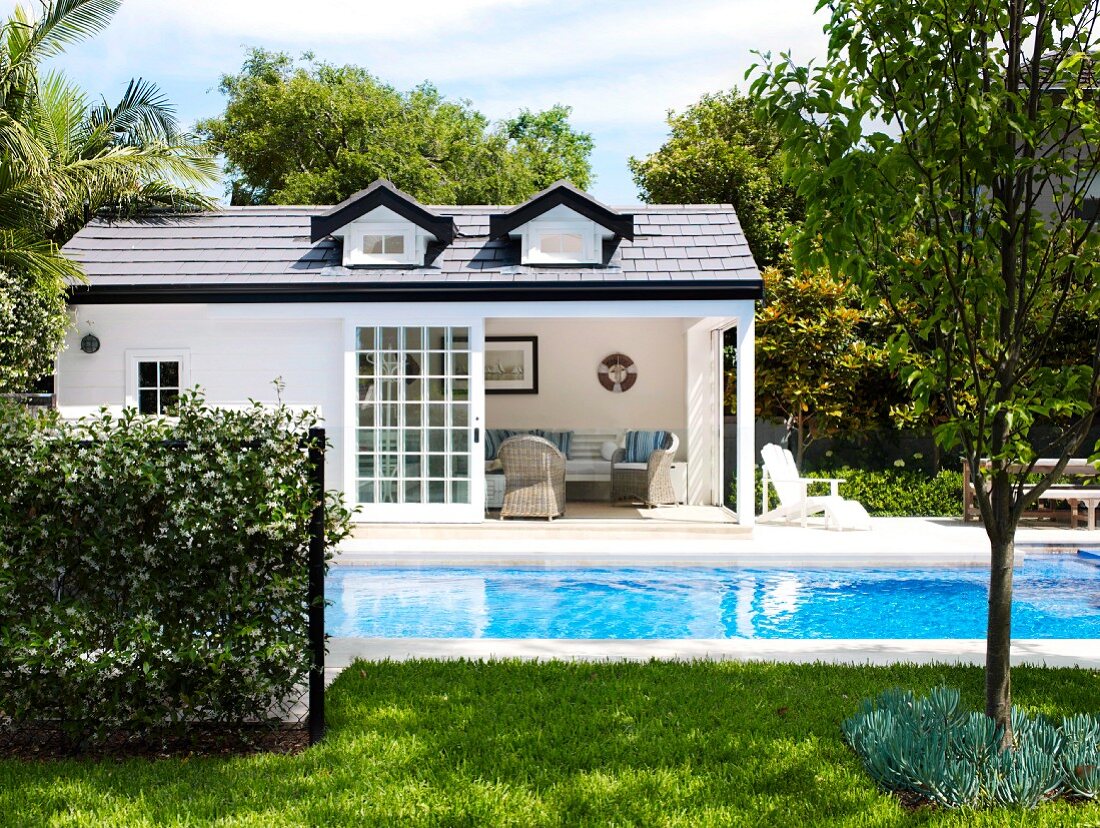 Large swimming pool in extensive garden; white summer house with open terrace doors in background