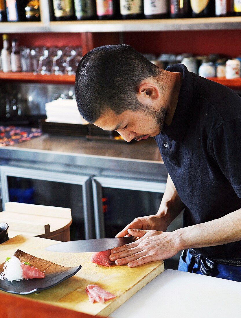 Japanischer Koch mit scharfem Messer, rohes Fischfilet schneidend