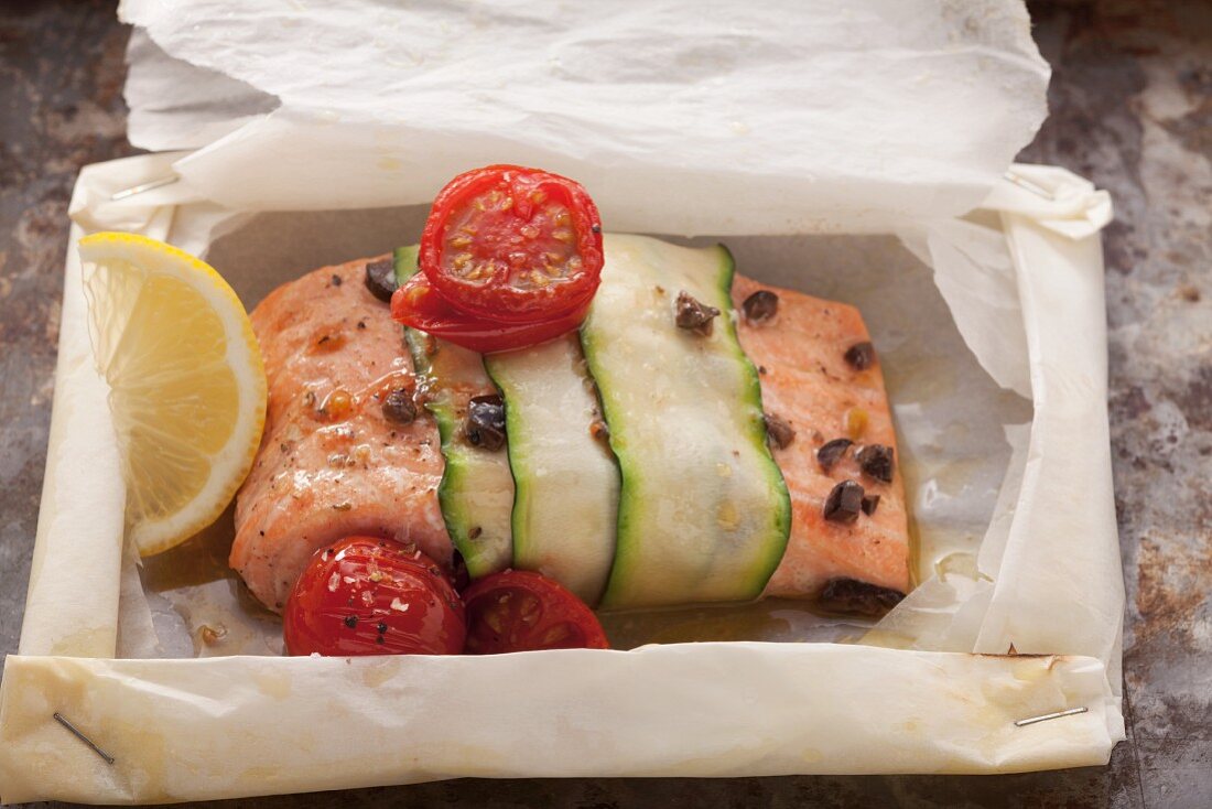 Salmon fillet wrapped in courgette with cocktail tomatoes and lemons on baking paper
