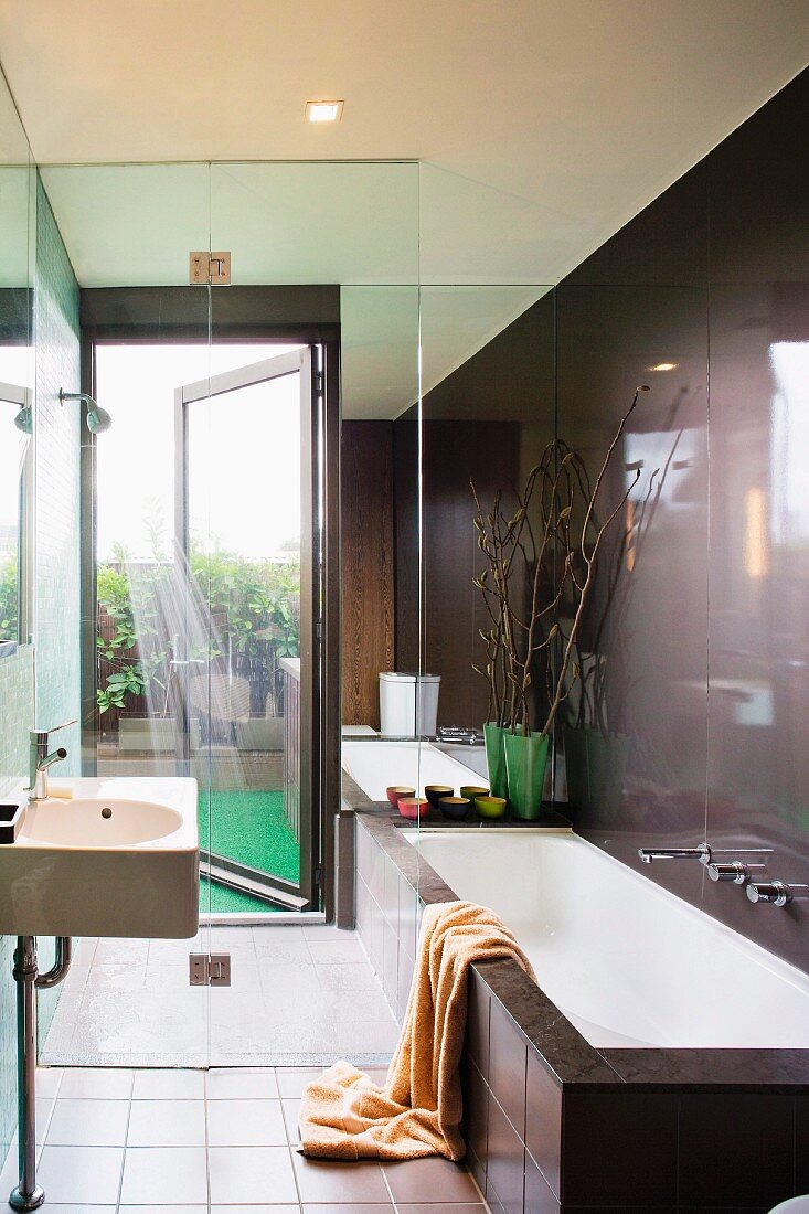 Designer bathroom in dark brown - wash basin and bathtub in front of a glass shower stall with access to the terriace