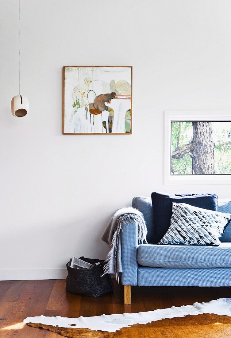 Polstersofa mit Kissen vor weißer Wand mit Fenster und Bild