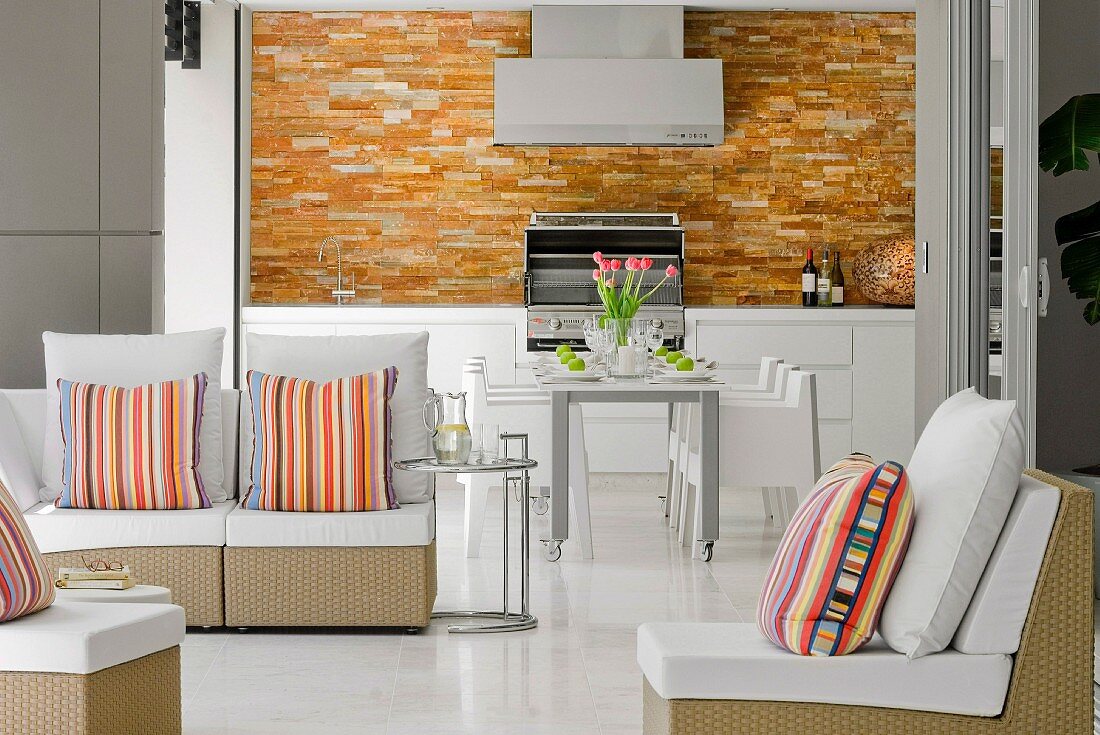 Wohn- und Eßbereich mit Designermöbeln überwiegend in weiß, Farbakzent durch geflieste Küchenwand und bunt gestreifte Sofakissen