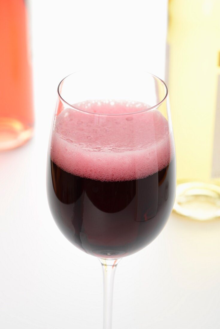 Moussierender Rotwein im Glas; im Hintergrund Weißwein und Rosewein