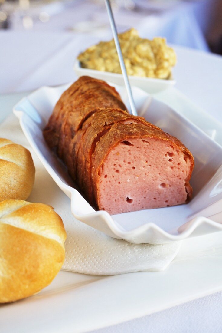 Sliced meat loaf with bread rolls and onion mustard