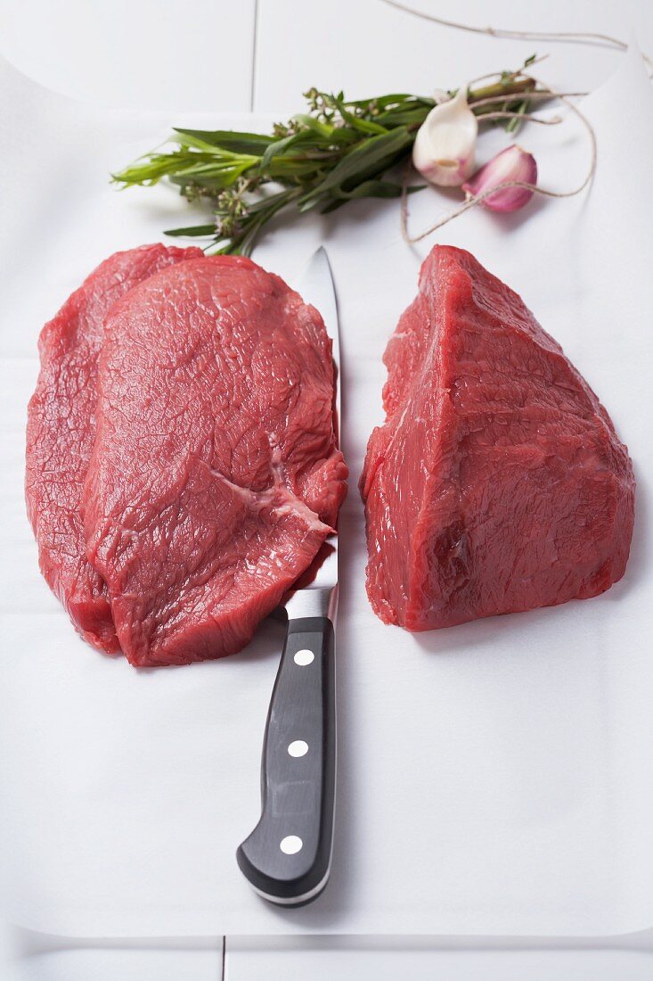 Steaks on baking paper with a knife, herbs and garlic
