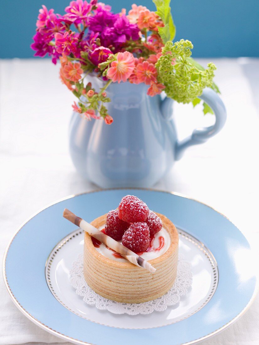 A raspberry tartlet and a bunch of flowers in a jug