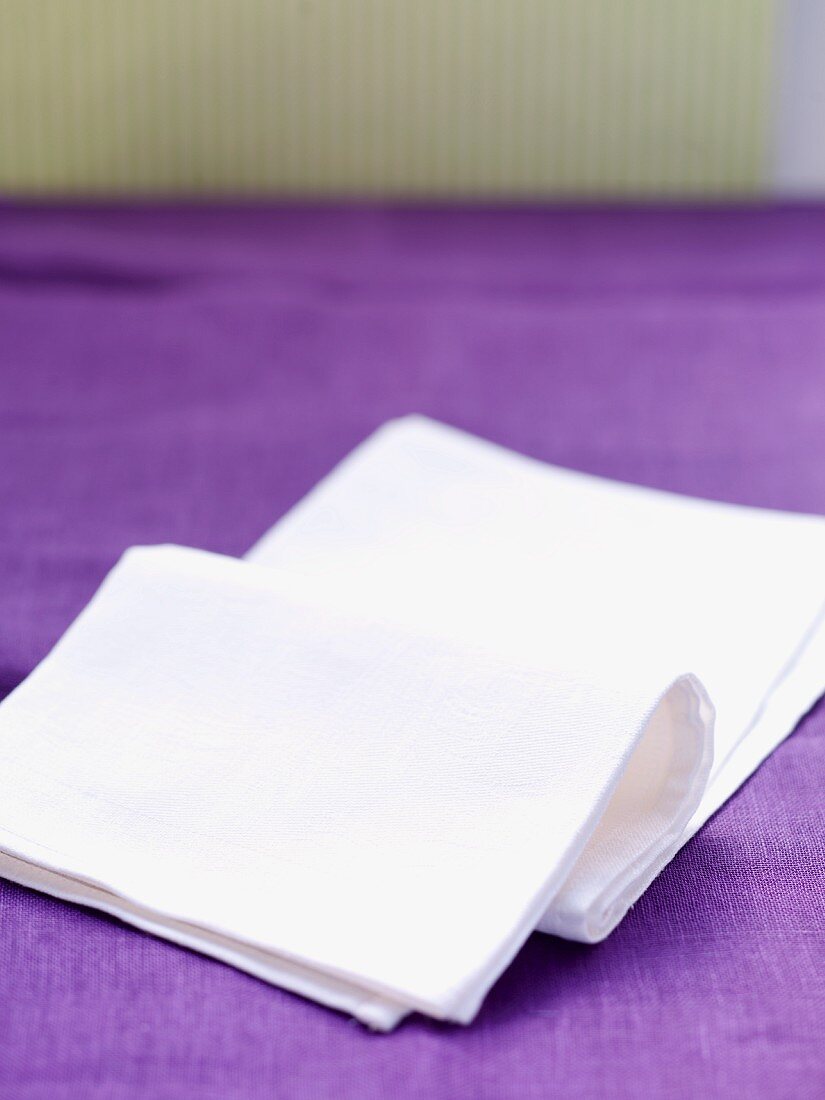 weiße Stoffserviette auf lilafarbener Tischdecke liegend