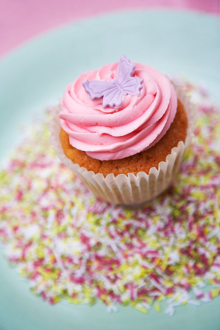 A cupcake decorated with pink frosting and a marzipan butterfly