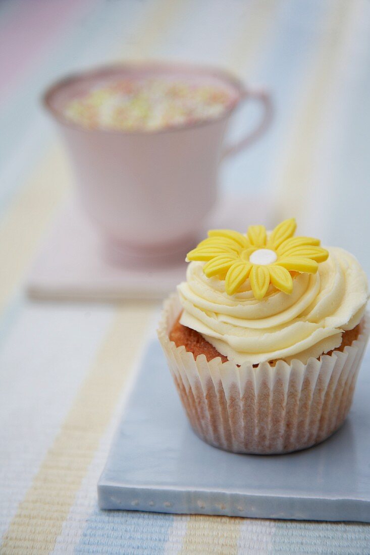 A cupcake decorated with light frosting and a marzipan flower
