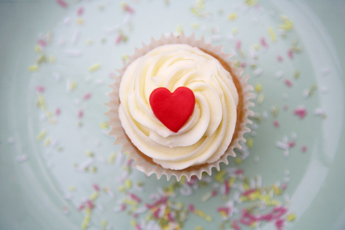 A cupcake decorated with light frosting and a red marzipan heart