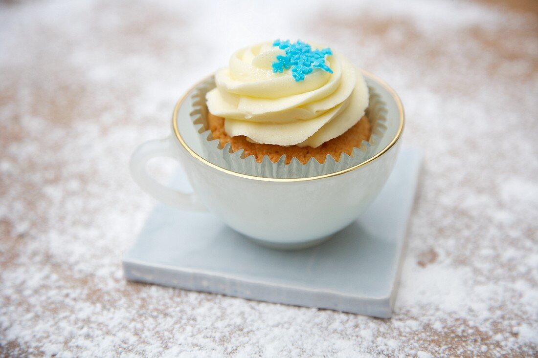 A cupcake decorated with light frosting and a sugar snowflake in a cup
