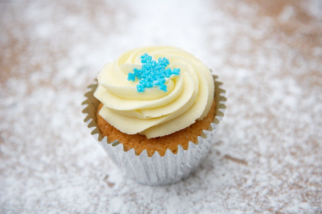 A cupcake decorated with light frosting and a sugar snowflake