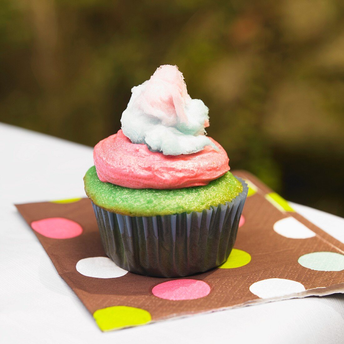 Grüner Cupcake mit rosa Frosting und Zuckerwatte
