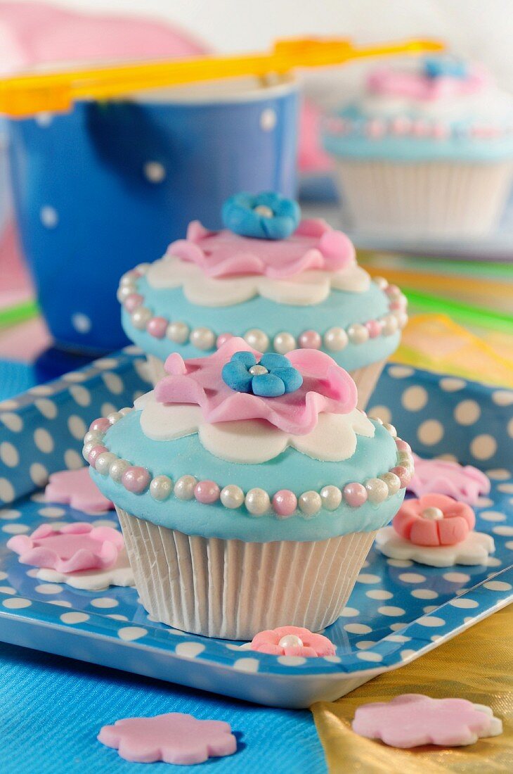 Hellblaue Cupcakes mit rosa Blüten und Zuckerperlen
