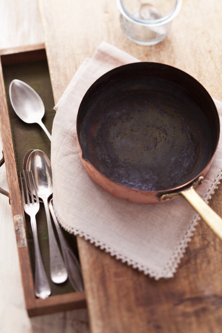 A copper pot on a wooden table with an open cutlery drawer
