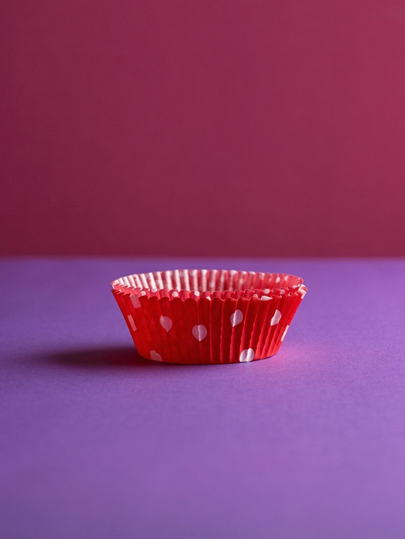 A muffin case on a purple surface against a pink background