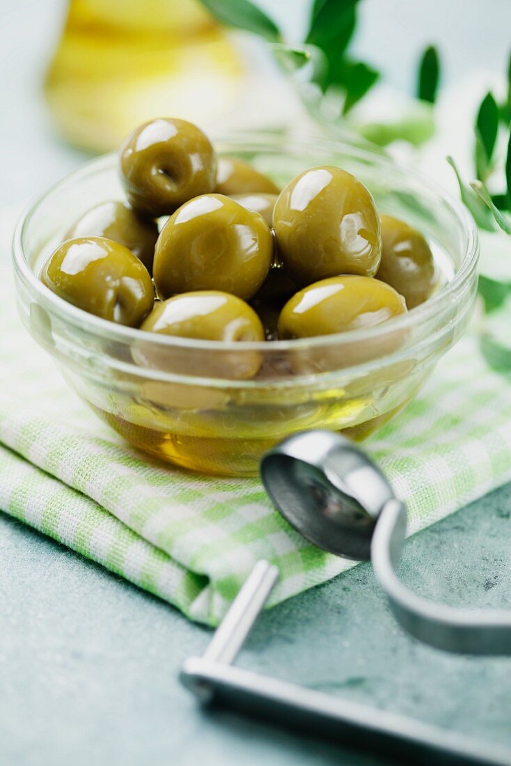 Grüne Oliven in einer Schale, daneben Entkerner