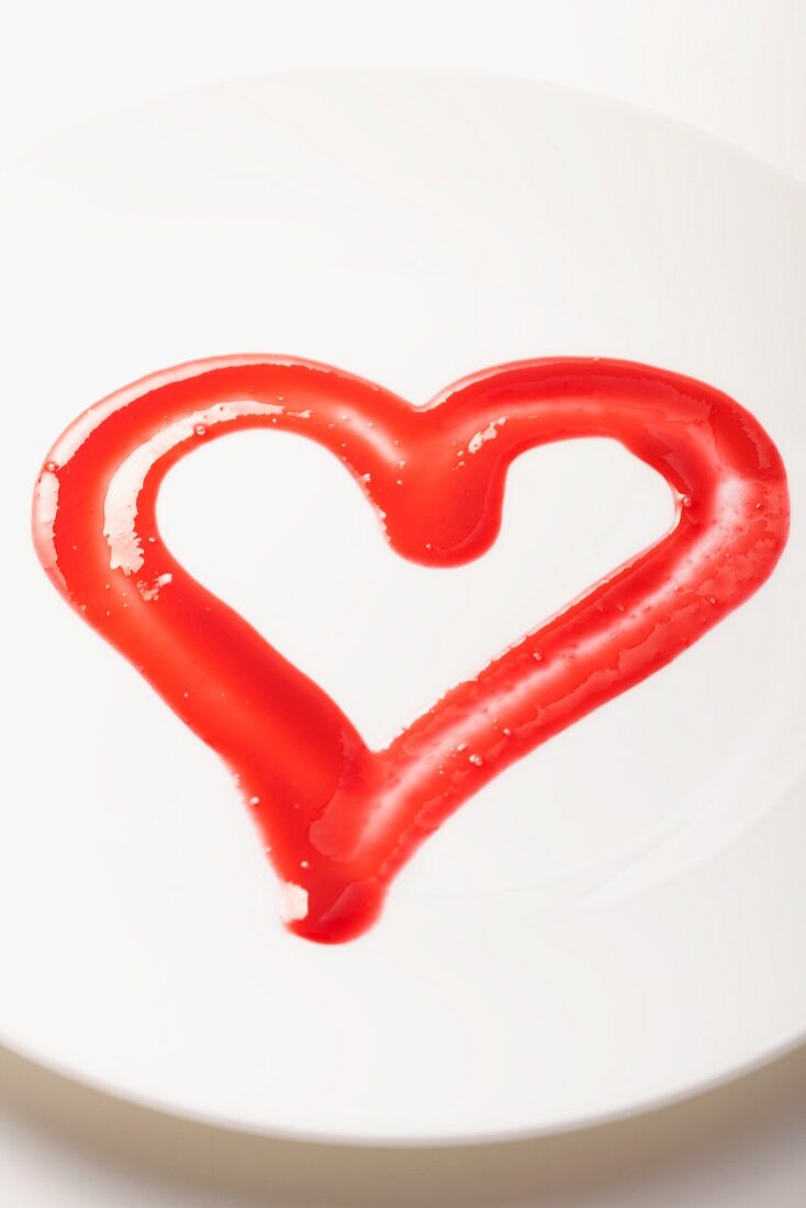 A red fruit sauce heart on a white plate
