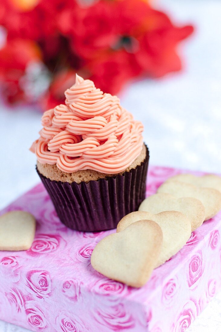 Vanille-Cupcake mit Erdbeer-Frosting, umgeben von herzförmigen Keksen
