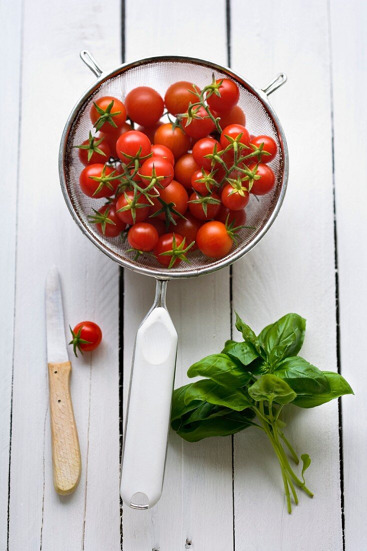 Cherry tomatoes in a sieve with a bunch of fresh basil next to it