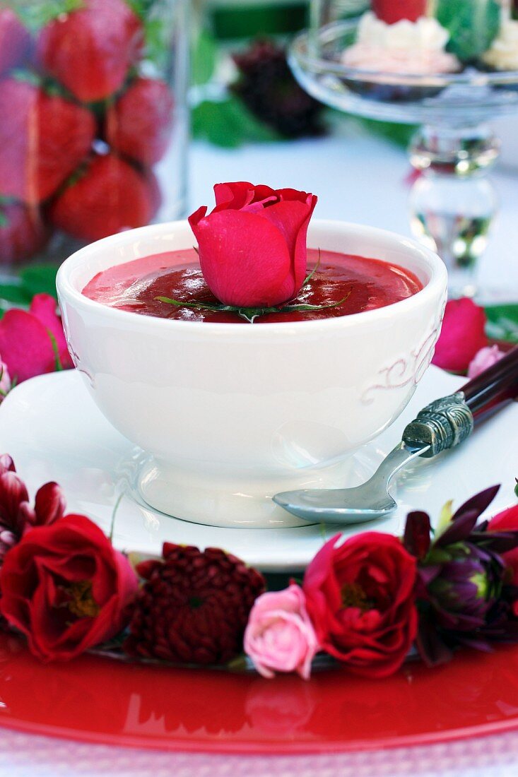 Erdbeerschale mit roter Rose und Blumenkranz um den Teller