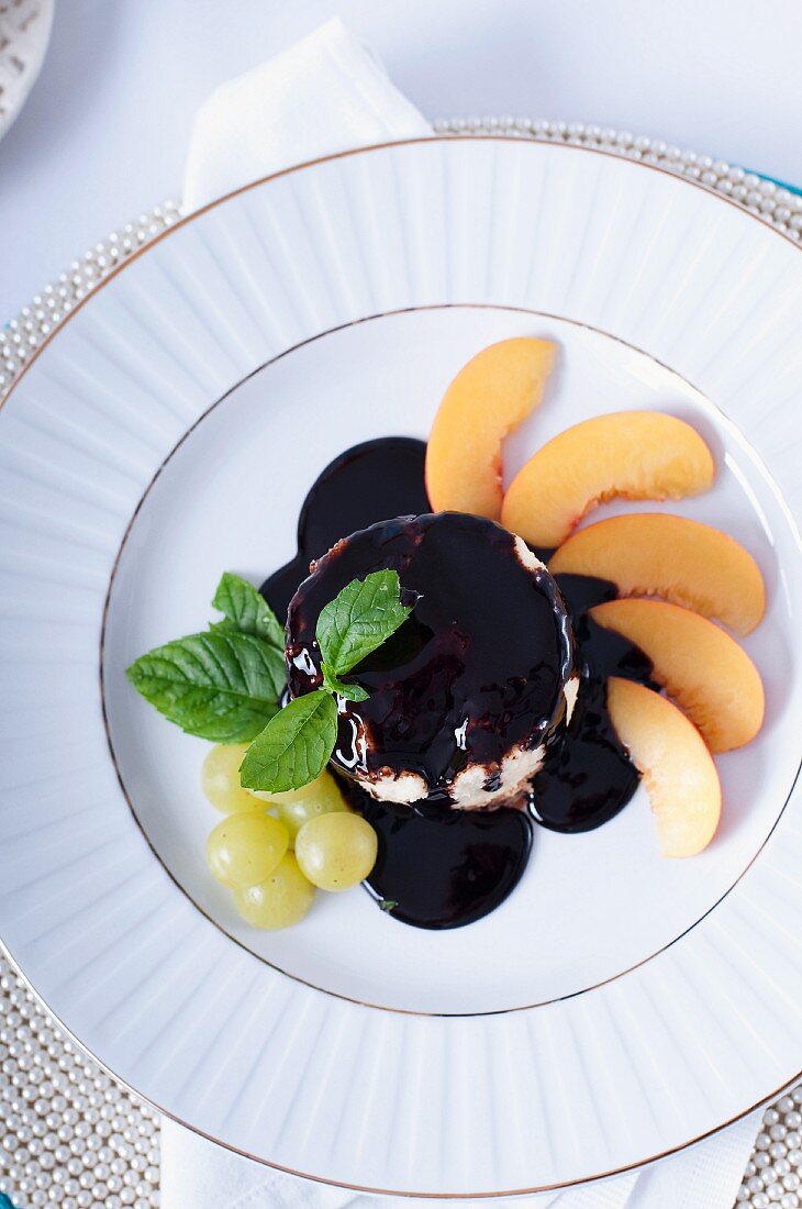 A mini cheesecake with chocolate sauce, grapes and nectarines