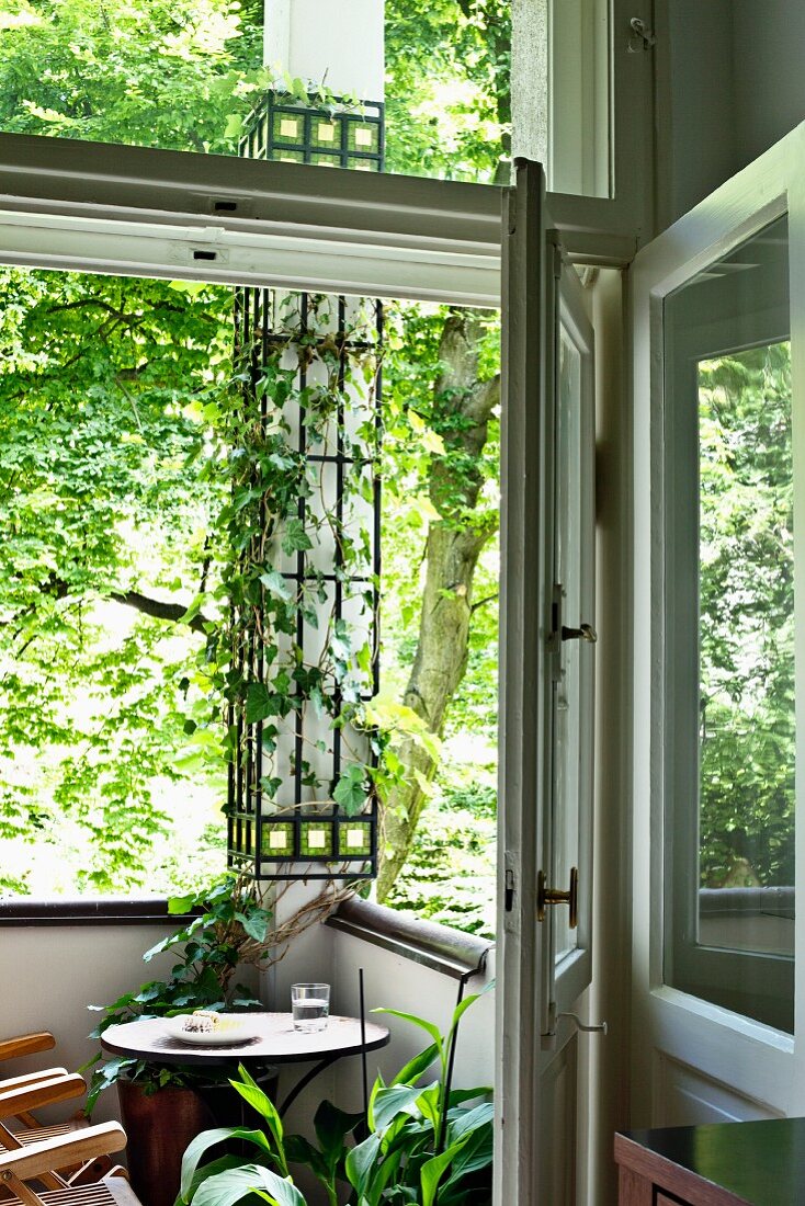 Blick durch offene Tür auf Bistrotisch in Balkonecke mit berankter Stütze