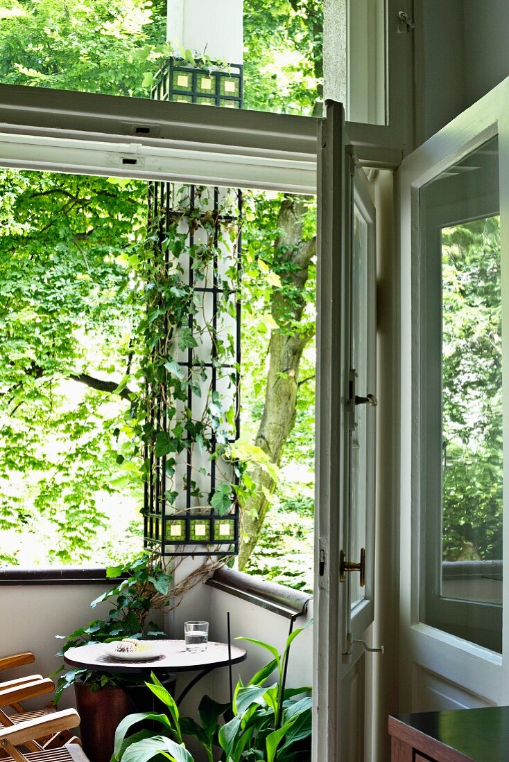 View of bistro table in corner of balcony with climber-covered pillar through open door