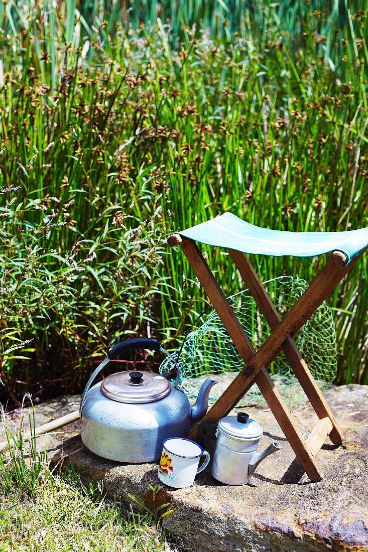 A folding stool and camping utensils on a rock outdoors
