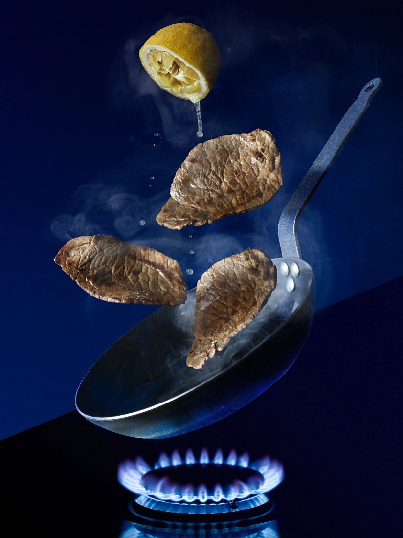 Escalopes in a pan on a stove being drizzled with lemon juice