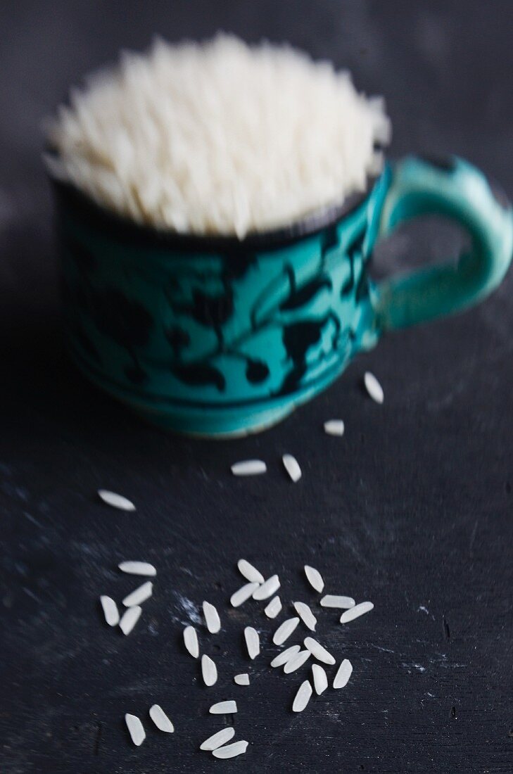 A cup of rice with rice strewn around it