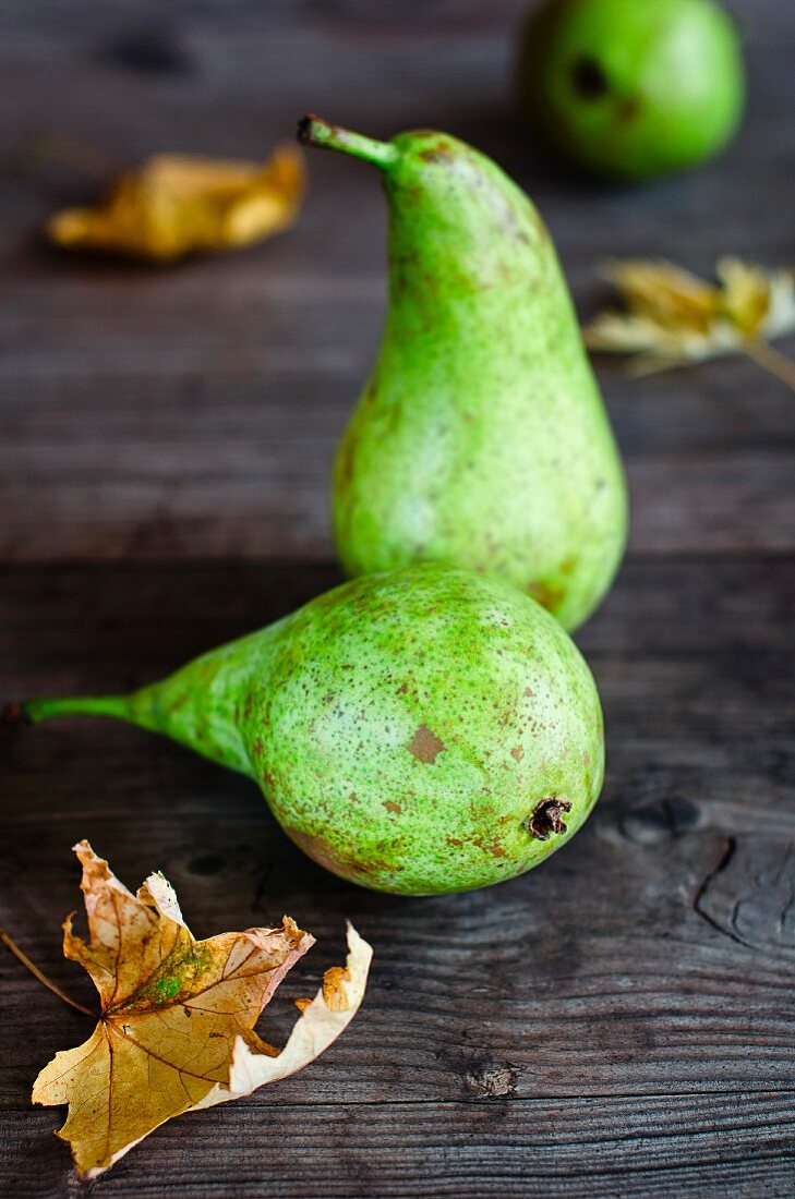 Green pears and autumnal leaves on a wooden surface