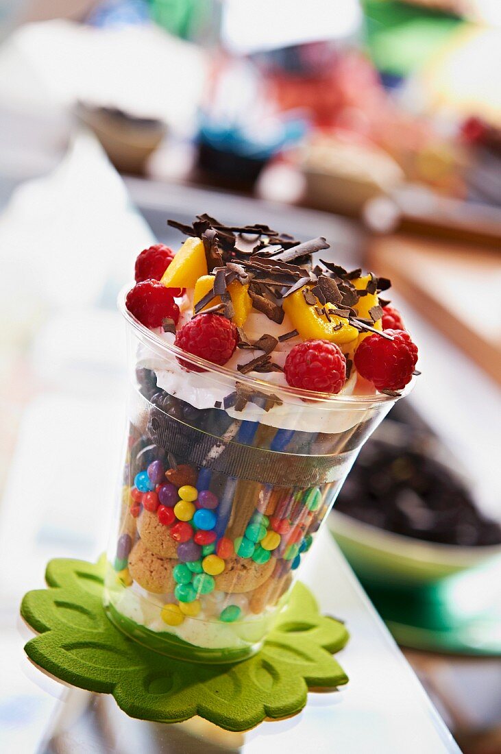 A colourful layer cup of biscuits, chocolate beans and raspberries