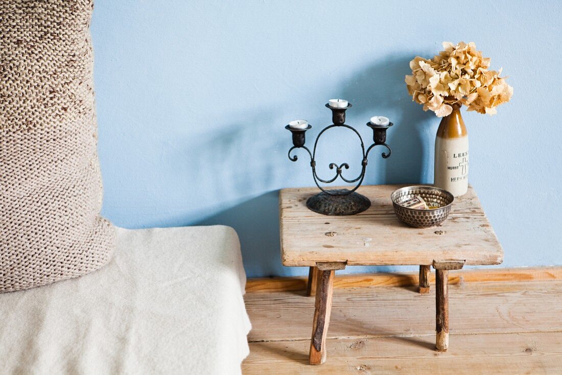 Candlestick and dried hydrangea on wooden footstool next to mattress