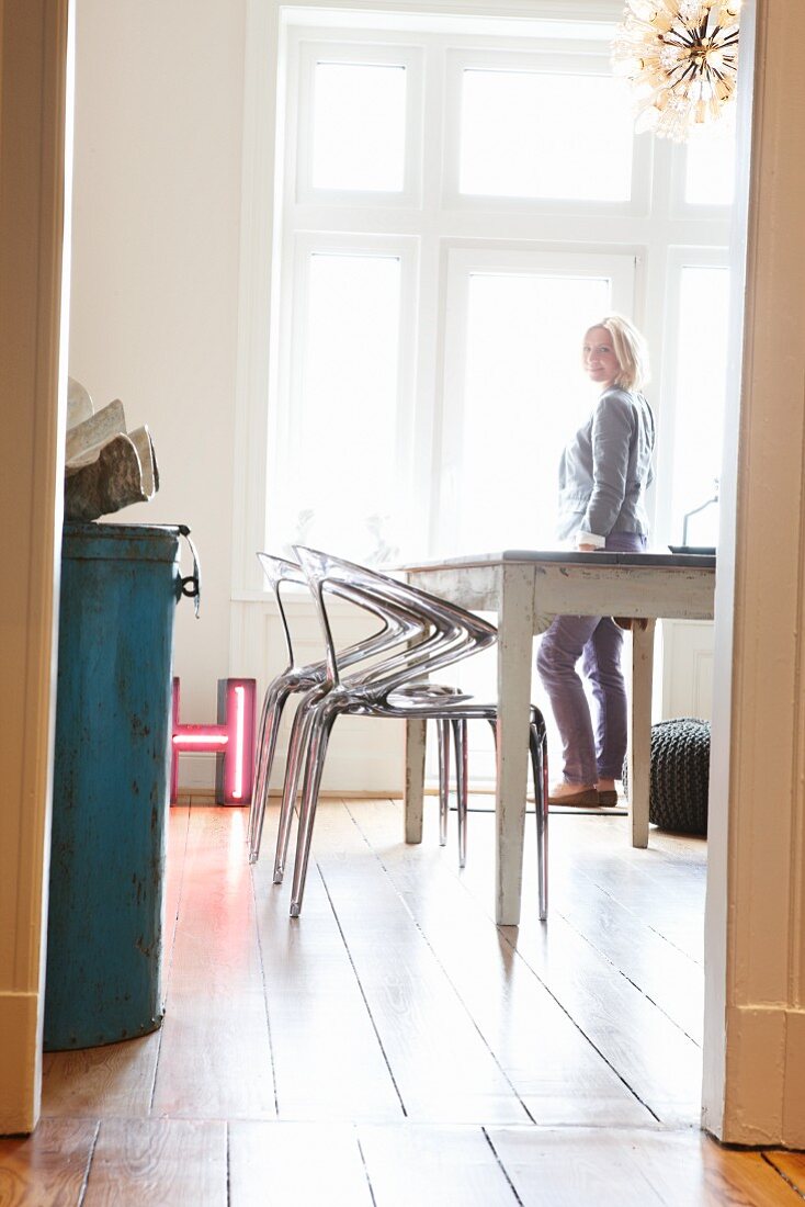 Postmoderne Acrylgas-Stühle und weisser Landhaustisch auf Dielenboden; Frau am Fenster