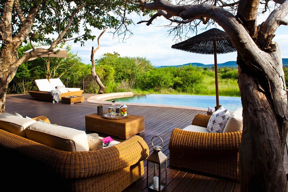 Holzterrasse mit Rattanmöbeln und anschliessendem Infinitypool in weiter Landschaft