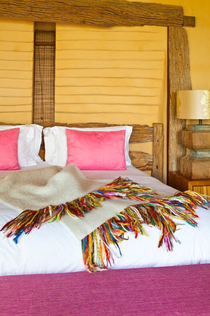 Bett mit pinkfarbenen Kissen an gelber Wand mit rustikalen Holzbalken