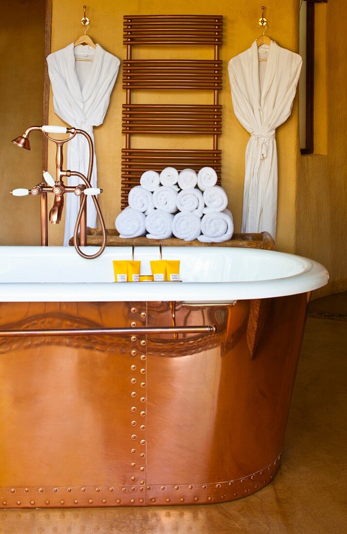 Exclusive copper bathtub with copper tap fittings; copper-coloured heated towel rail on wall in background