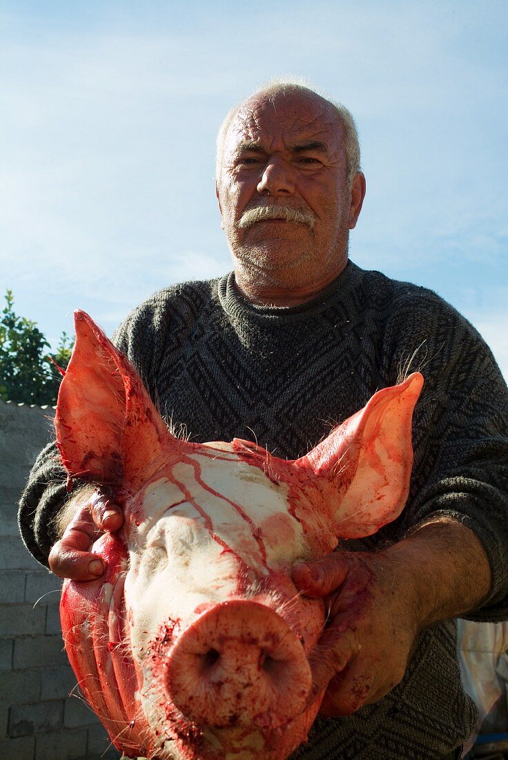 Metzger hält einen Schweinekopf