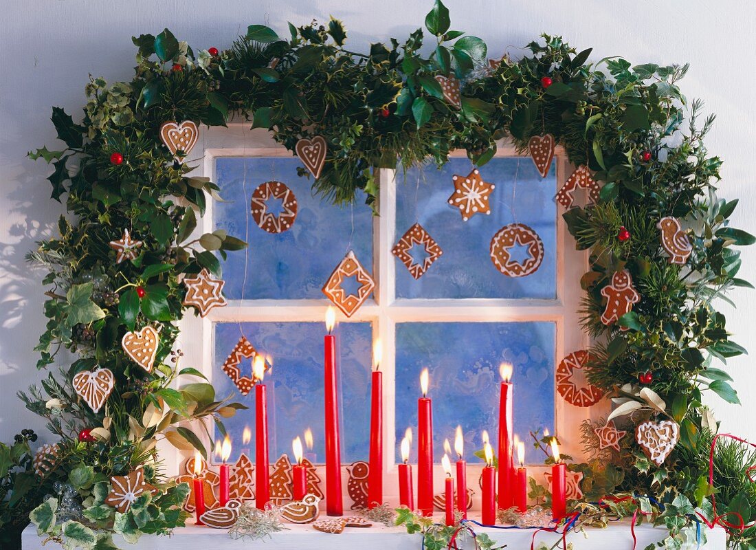 A window decorated with a garland, burning candles and Christmas biscuits