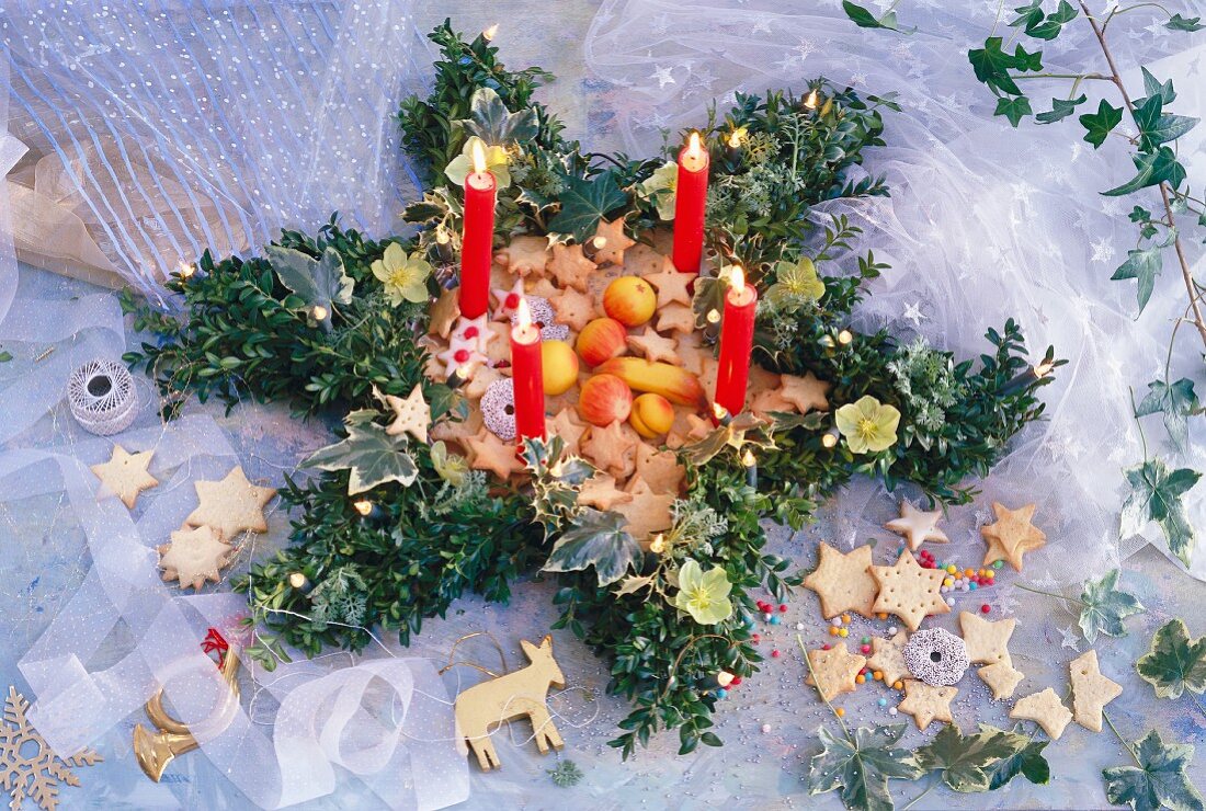 Weihnachtskranz aus Buchsbaum, Stechpalme, Efeu und Christrosen mit Kerzen, gefüllt mit Weihnachtsplätzchen und Marzipanobst