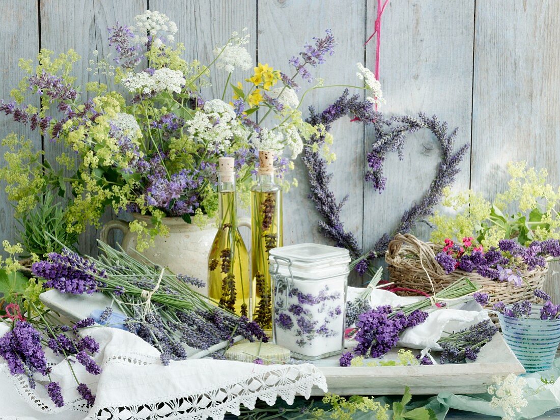 An arrangement of lavender: a heart-shaped lavender wreath, a jar of lavender sugar, two bottles of lavender and olive oil, wild chervil and lady's mantle