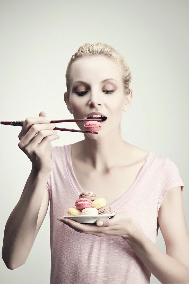 Junge Frau isst Macarons mit Essstäbchen