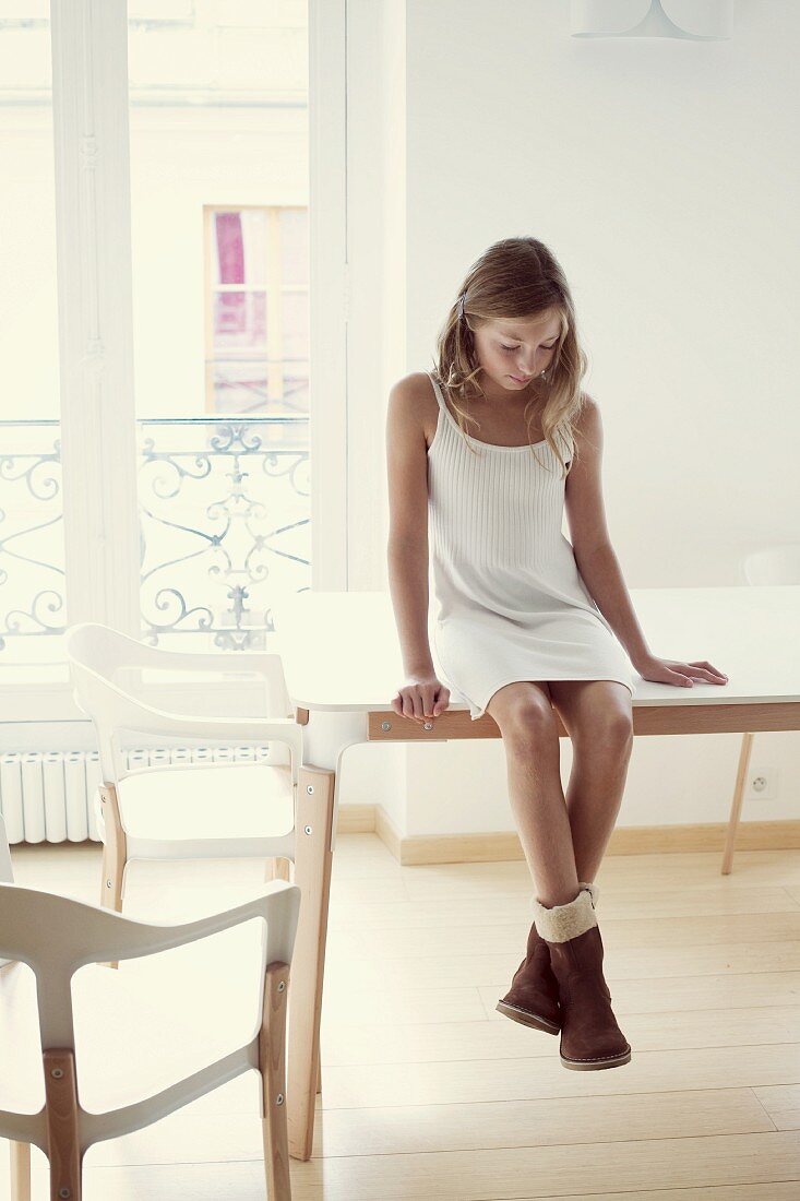 Mädchen in Kleid und Stiefeln sitzt auf einem Tisch im Zimmer