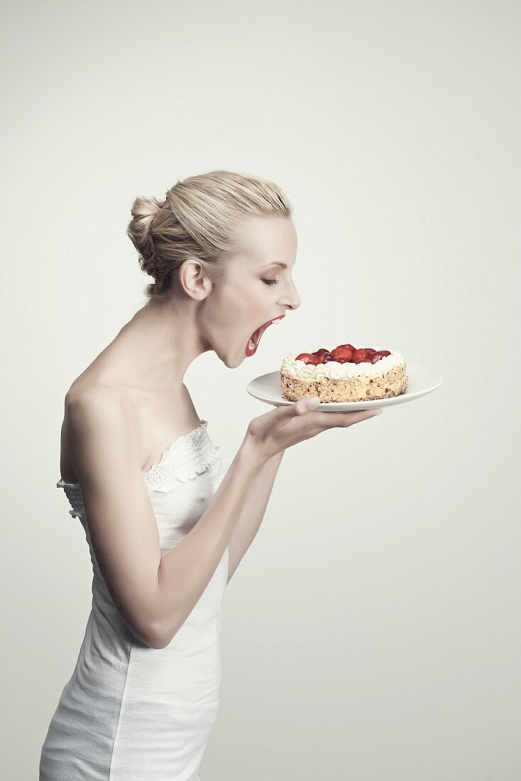 A young woman about to bite into a strawberry cake