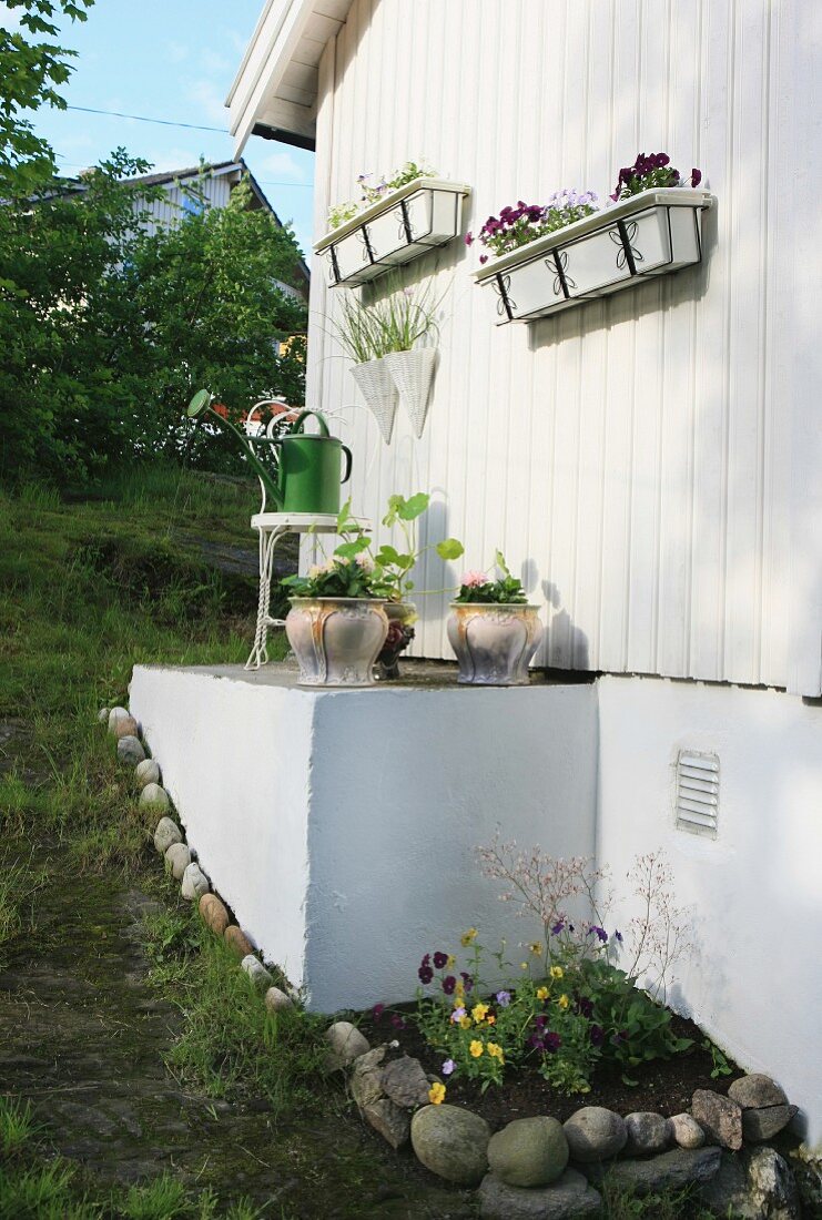 Dekorierte Hausfassade eines weissen Holzhauses mit weissen Blumenkästen und Blumentöpfen