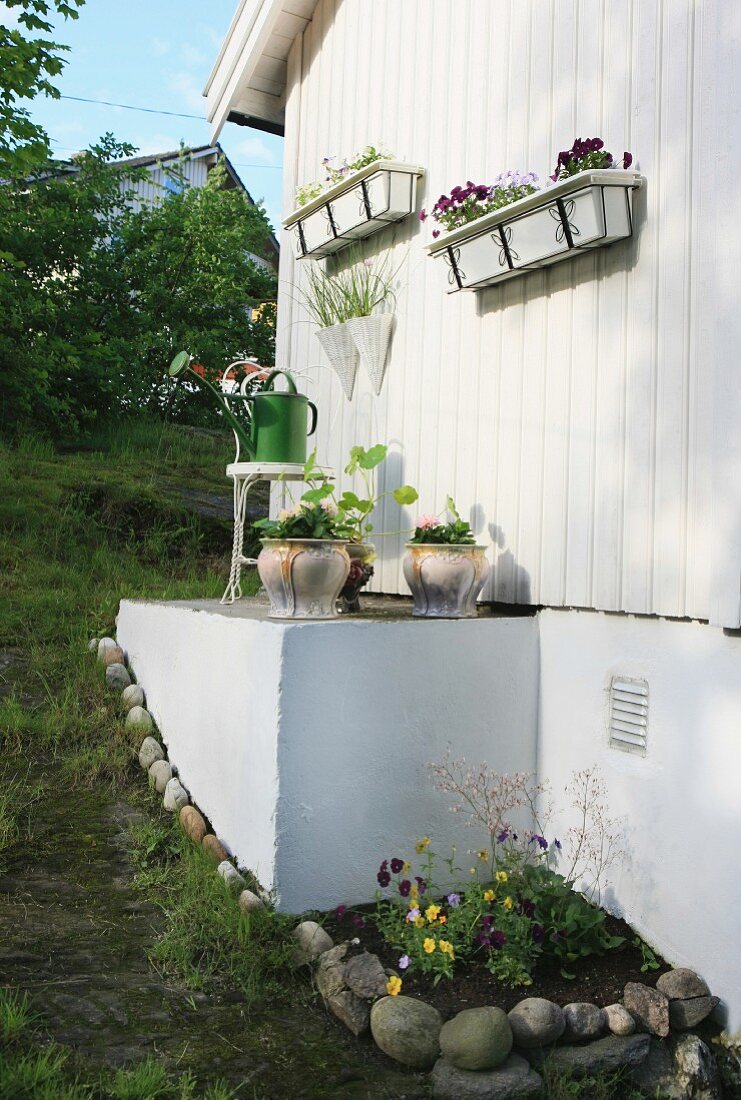 Facade of white wooden house decorated with white window boxes and planters