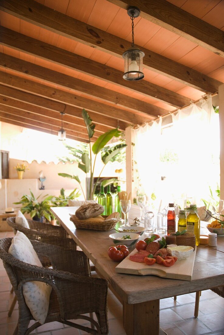 A patio table laid for a Mediterranean snack on the veranda under a wooden roof