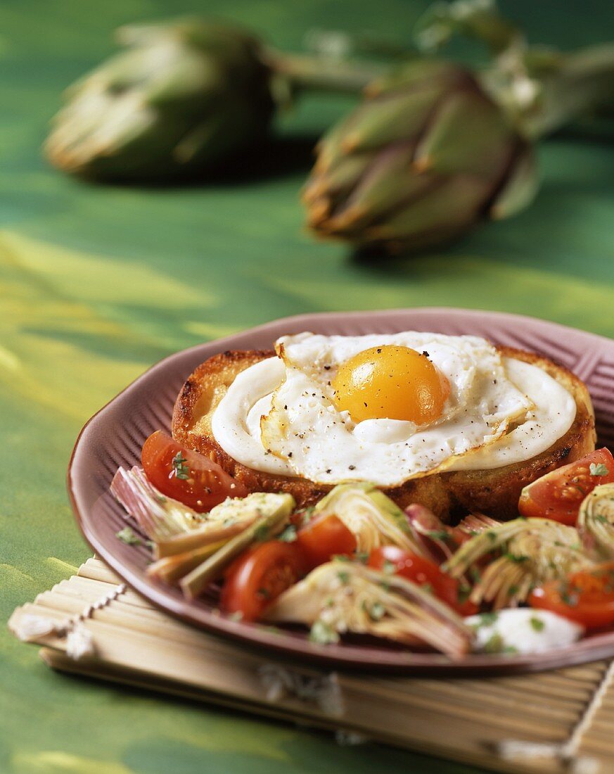 A fried egg on toast with grilled tomatoes and artichokes